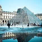 Iconic glass pyramid of the Louvre Museum in Paris reflecting in a pool, showcasing classic architecture.