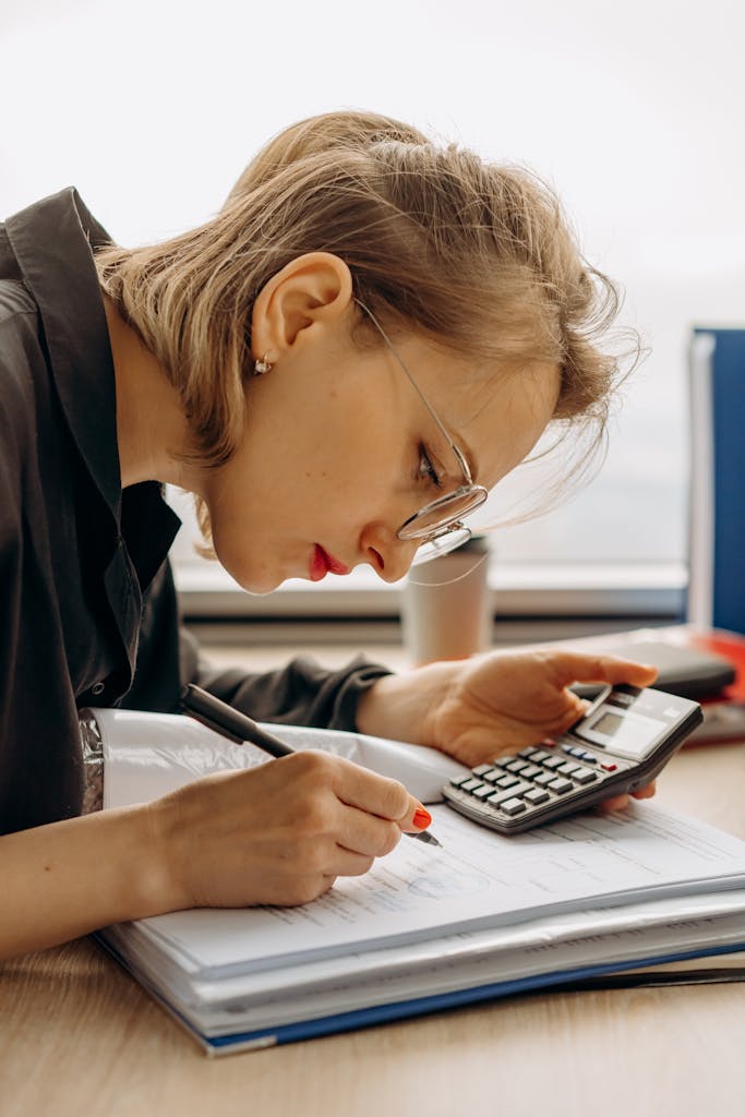 Woman with eyeglasses concentrating on financial calculations with notebook and calculator.