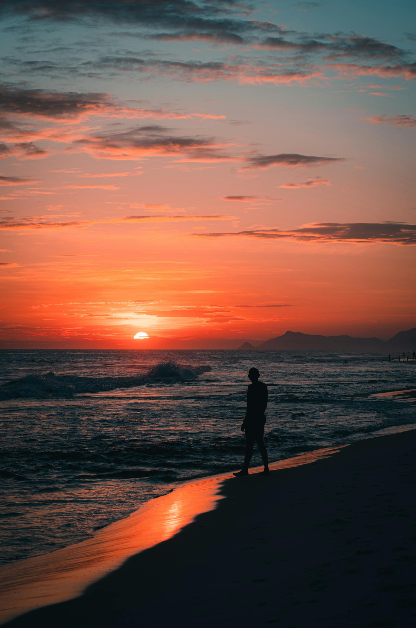 A person walking along the beach at sunset in Rio de Janeiro, Brazil, with a dramatic sky.