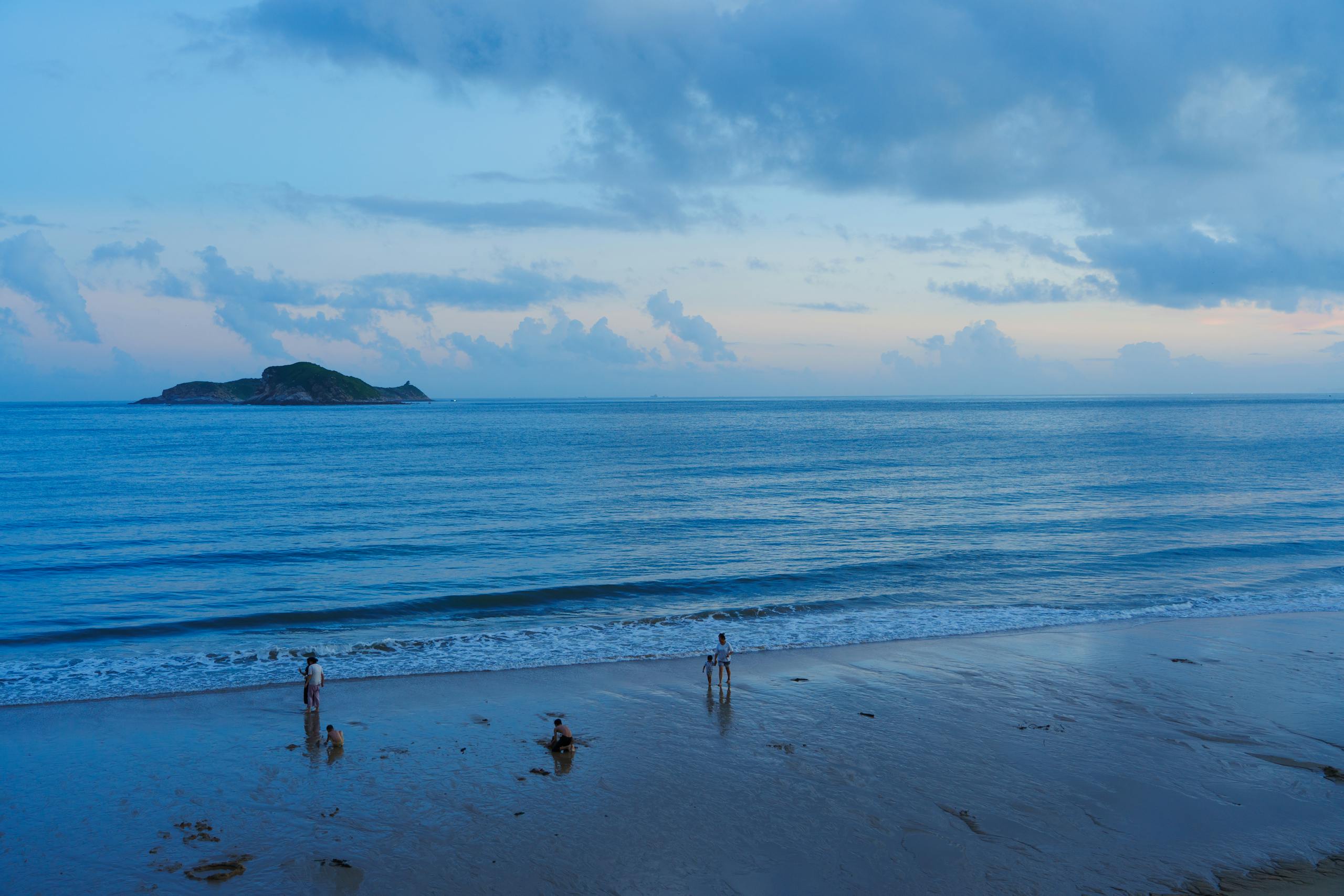 Peaceful beach scene with people enjoying the sunset by the ocean and distant island.